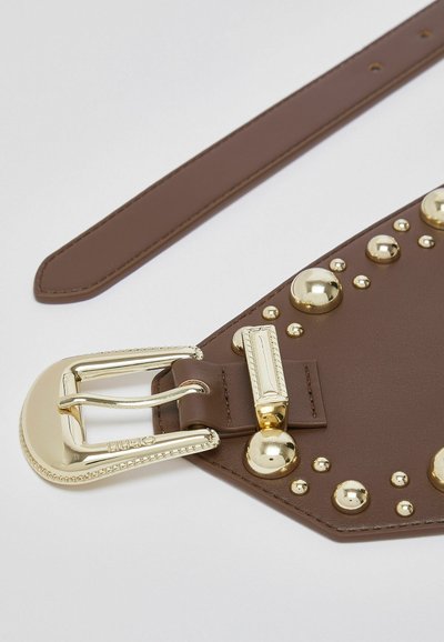 Ceinture en cuir marron avec boucle couleur or et clous décoratifs dorés sur une large section sur fond blanc.