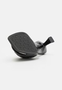 Calzado negro con suela de goma texturizada, que presenta una plataforma ancha y un tacón redondeado para la estabilidad. Diseño elegante y minimalista.