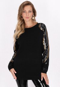 Pulover negru cu mâneci lungi, prezentând modele de valuri din paiete aurii și argintii pe mâneci. Textură moale, guler rotund, croială lejeră.