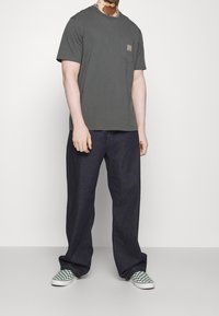 Ciemnoszara bawełniana koszulka z kieszenią na piersi. Połączona z ciemnymi jeansami i zielonymi, kratkowymi butami wsuwanymi. Prosty, casualowy design.