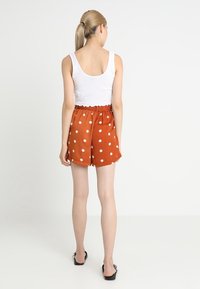 Pantaloni corti arancioni a pois con cintura elastica, realizzati in tessuto leggero. Esibiti con una canotta bianca e sandali piatti.