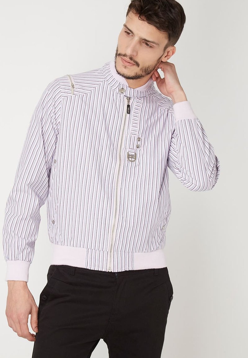 Chaqueta bomber a rayas en lavanda claro y blanco con puños acanalados, cuello alto, cierre de cremallera y bolsillo lateral con cremallera.
