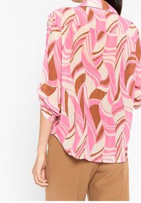 Löst sittande blus i lätt material, med ett abstrakt vågmönster i rosa, brunt och kräm, med uppvikt ärm och en böjd nederkant.