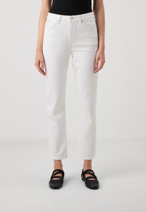 Jean en denim blancs taille haute avec une coupe droite, comportant cinq poches et des coutures contrastées. Associés à des chaussures plates noires.