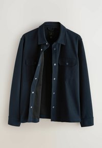 Veste-chemise bleu foncé à manches longues avec col, boutons-pression et deux poches poitrine, montrée partiellement ouverte sur un fond clair.