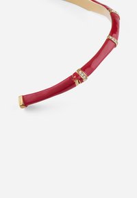 Fascia rossa lucida con accenti in metallo dorato e piccoli cristalli trasparenti. Presenta un design curvo e segmentato per maggiore flessibilità.