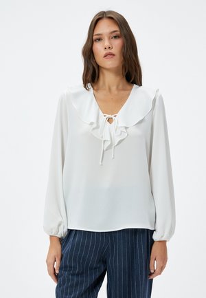 Witte blouse met een gerimpelde kraag en striksluiting, lange mouwen met gathered manchetten, gemaakt van een soepele stof, gedragen met gestreepte broek.
