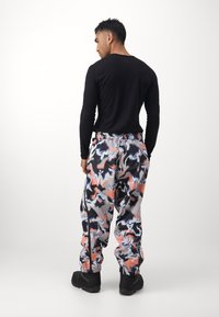 Μαύρο πουκάμισο με μακριά μανίκια συνδυασμένο με παντελόνι με χρωματιστό, αφηρημένο σχέδιο σε αποχρώσεις του ροζ, μπλε και μαύρου, με ελαστικούς σφιγκτήρες και φερμουάρ στα πλάγια.