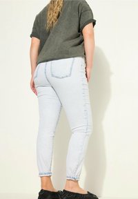 Svetle modré úzké džíny s vybledlým vzhledem, ohrnutými nohavicemi a klasickým pěti-kapsovým designem. Kombinováno s tmavě zeleným oversized tričkem.