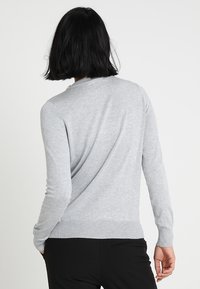 Pull gris clair en tissu doux, avec un col arrondi, des manches longues, des poignets et un ourlet côtelés, offrant une coupe décontractée.