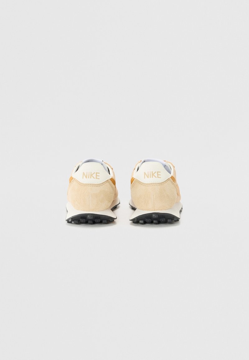 Baskets Nike avec une tige en suède beige clair, des détails blancs et une semelle intercalaire en caoutchouc noir avec un motif de traction texturé.