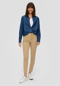 Koszula zapinana na guziki z dżinsu, khaki spodnie slim-fit i białe trampki. Niebieska koszula z klasycznym kołnierzykiem, lekkiego materiału i gładkiej tekstury. Prosty design.