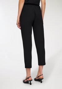 Czarne spodnie z gumką w talii o dopasowanym kroju, skróconej długości i z podwiniętymi mankietami, zestawione z czarnymi sandałami na obcasie z paskami.
