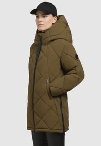 Olivengrüner gesteppter Parka mit hohem Kragen, der über einen Reißverschluss, Eingrifftaschen und schwarze Akzente, einschließlich einer Kapuze und einem Logo-Patch, verfügt.