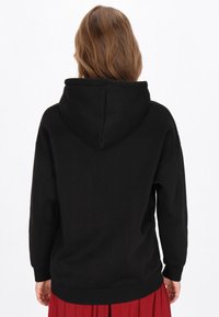 Sudadera con capucha negra que presenta una capucha grande, hombros caídos y un dobladillo con detalles acanalados, hecha de una tela suave y texturizada.