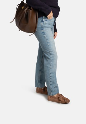 Lichtblauwe jeans met rechte pijpen en rafelige zoom, gecombineerd met bruine suède mocassinachtige schoenen en een bruine leren handtas.