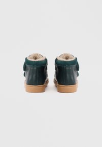 Grüne Leder-High-Top-Schuhe mit tanfarbenen Gummisohlen und weicher beigefarbener Fütterung. Verfügt über seitliche Riemen und eine glatte, matte Oberfläche.