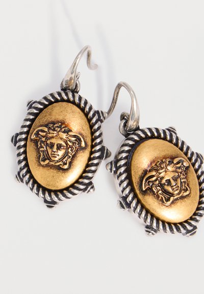 Ασημένια και χρυσά οβάλ σκουλαρίκια με ανάγλυφη κεφαλή Μέδουσας στο κέντρο, περιβαλλόμενα από λεπτομέρειες στριμμένης ασημένιας σχοινίδας και γάντζους για να φοριούνται.