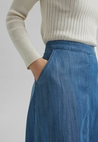 Jeanskjol i blått med vida form, utrustad med sidofickor och subtil textur. Toppen är en krämfärgad ribbad tröja med långa ärmar.