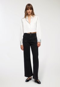 Krótka biała satynowa bluzka z guzikami i długimi rękawami, połączona z czarnymi, szerokimi jeansami o wysokim stanie z kieszeniami naszytymi. Czarne baleriny.