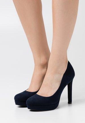 Granatowe zamszowe czółenka na wysokim obcasie z okrągłym noskiem i platformą, charakteryzujące się gładką teksturą oraz smukłym obcasem typu stiletto.