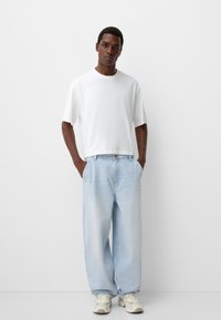 Weißes T-Shirt mit kurzen Ärmeln, kombiniert mit hellblauen, lockeren Jeans und cremefarbenen Sneakers. Lässiges Design, entspannter Schnitt und glatte Textur.
