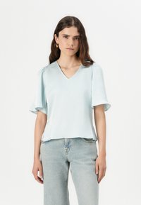Top azzurro chiaro a maniche corte con scollatura a V e dettaglio di spalline arricciate, abbinato a jeans in denim chiaro a vita alta. Texture morbida.