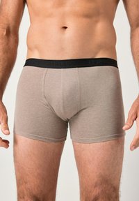 Boxer breves de algodón marrón con una cinturilla elástica negra que presenta texto grabado. La tela tiene una textura suave y un diseño ajustado.