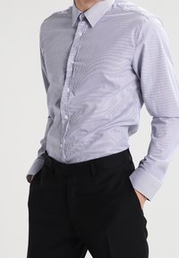 Skjorta med knappar i ljusblå och vita ränder; långärmad, spetsig krage, mjukt tyg, matchad med svarta byxor.