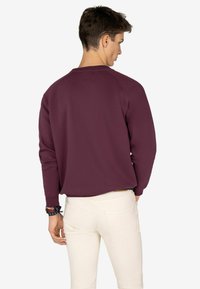 Sudadera burdeos con cuello redondo y mangas largas, con un color sólido y textura suave. Se combina con pantalones de tonos claros.