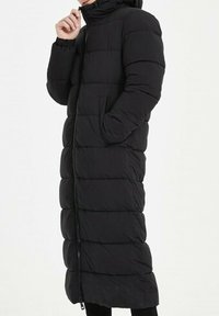 Manteau long noir matelassé avec col haut, design à coutures verticales et fermeture éclair à l'avant. Il dispose de poches latérales et de poignets élastiques.