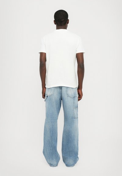 Tricou alb din bumbac cu mâneci scurte, asortat cu pantaloni cargo din denim lejeri, de culoare albastră deschis, cu buzunare și tiv desfăcut.