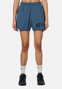Blå sportshorts med elastisk midja, prydda med en mörkgrön "ATM"-logga. Bärs med svarta sneakers och vita strumpor.