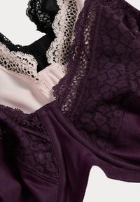 Zwei BHs mit einer Mischung aus Materialien: einer in dunklem Lila mit Spitzensaum, der andere in Rosa mit schwarzen Spitzenakzenten. Sichtbare strukturierte Designs.