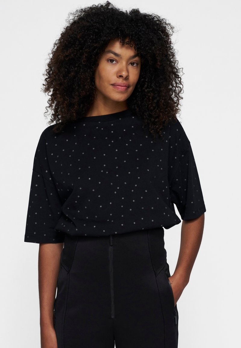 Sort T-shirt med korte ærmer, der har et prikket mønster. Fremstillet af blødt stof med en afslappet pasform og bådudskæring, kombineret med sorte bukser.