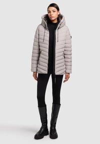 Polstret, lysegrå jakke med hætte, der har lodrette striber, frontlynlås og sidelommer. Matcher med sorte leggings og knæhøje støvler.