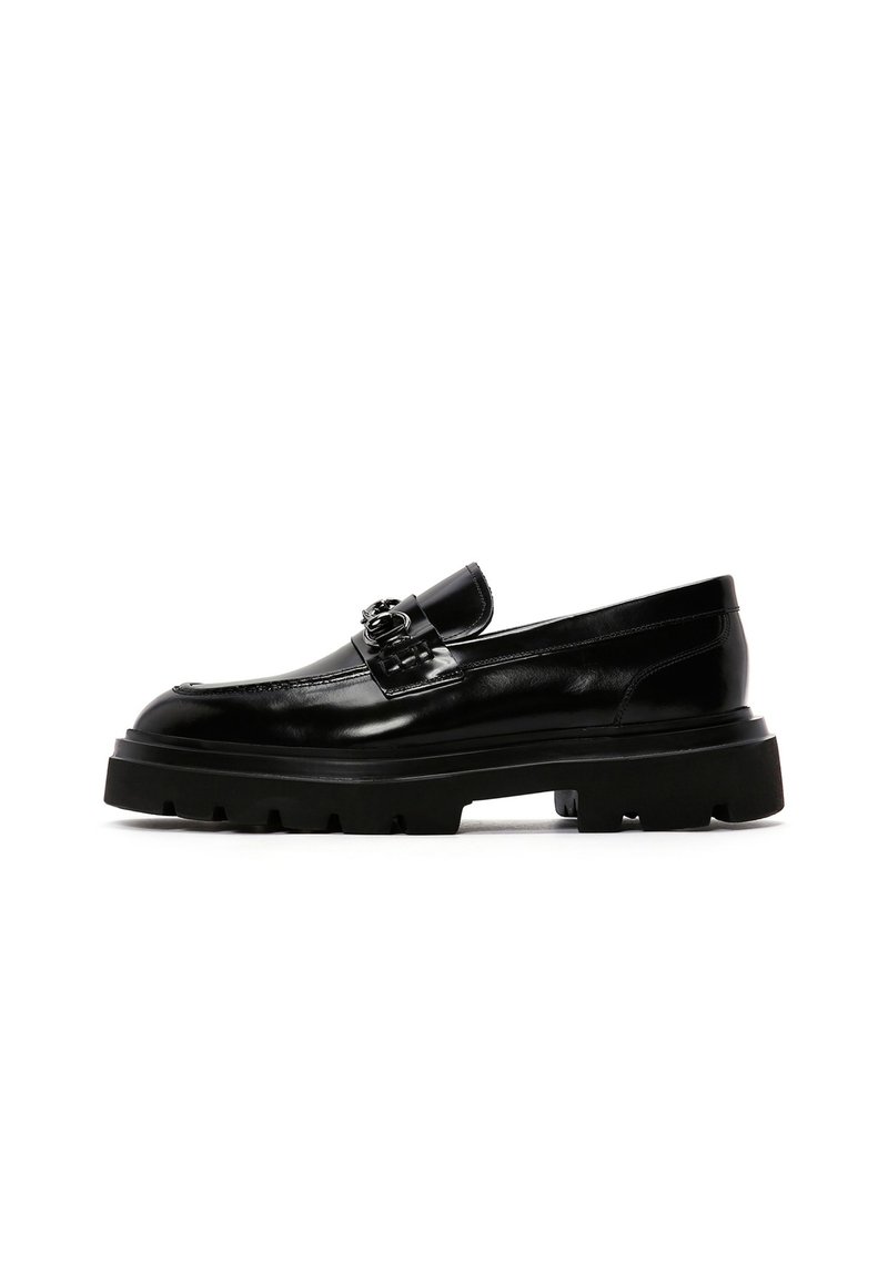 Mocasines de cuero negro con suela de goma negra gruesa, detalle decorativo de hebilla y acabado suave. Diseño clásico con acentos modernos.