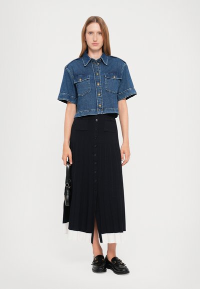 Kuttet denimskjorte med korte ermer og to frontlommer, sammen med et langt svart ribbestrikket skjørt med hvit kant og frontknapper.