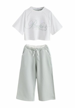 Top scurt alb cu mâneci scurte, cu textul „Baker by Ted Baker”, asortat cu pantaloni largi gri deschis cu șnur și buzunare laterale.