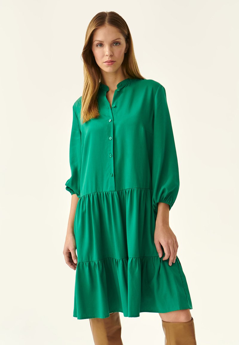 Vestido verde abotonado en tela ligera, con mangas largas tipo globo, falda en capas y cuello redondeado.
