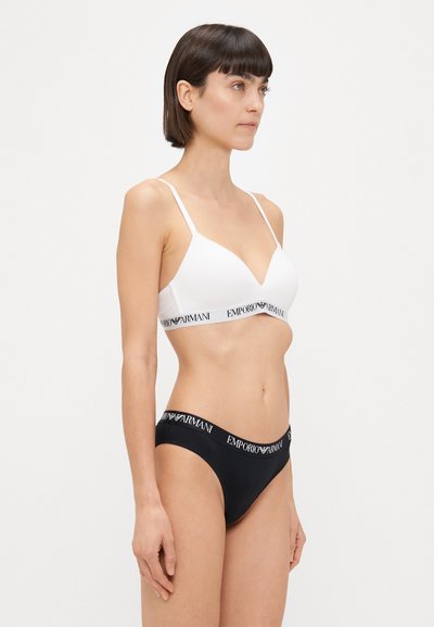 Bralet alb cu decolteu în V, bretele ajustabile și bandă cu logo negru, asortat cu chiloți bikini negri care au talie cu logo corespunzător.