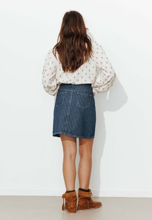 Jupe en jean rayée verticale, couleur bleu foncé, taille haute, associée à des bottines en daim marron avec des accents de pompons.