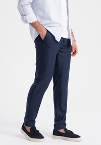 Pantalons joggers bleu marine, fuselés en tissu doux, dotés de poches latérales et d'une texture lisse. Associés à des chaussures à enfiler sombres.