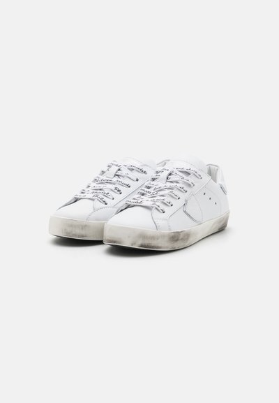 Fehér bőr sneakers, lapos talppal, kontrasztos részletekkel és díszes fűzőkkel, kézzel írt szöveggel. A talp enyhén kopott kinézete.