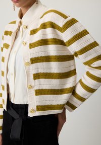 Gehaakte cardigan in roomkleur met groene strepen, voorzien van een ronde kraag, textuurstof en gouden decoratieve knopen.