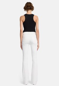 Schwarzes ärmelloses Top kombiniert mit weißen, ausgestellten Jeans, die eine hohe Taille und Taschen auf der Rückseite haben. Glatte Textur und figurbetonte Silhouette.