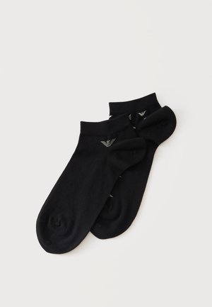 Paire de chaussettes courtes noires avec petit logo blanc sur les bords côtes, posées à plat sur un fond clair.