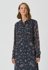 Rochie cu imprimeu floral, cu mâneci lungi, de culoare bleumarin, cu închidere prin buton, care prezintă pliuri și flori roz și albastre răspândite pe un material transparent.