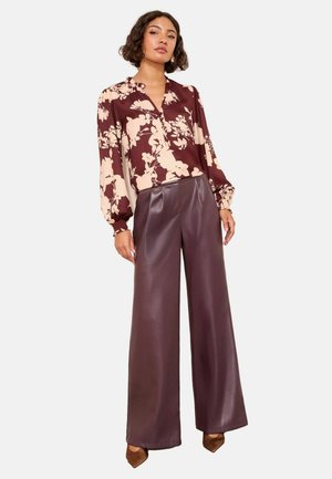 Langarm blouse met een maroon bloemenpatroon op een beige achtergrond. Gecombineerd met hooggewaiste, wijde burgundy nep-lederen broek.