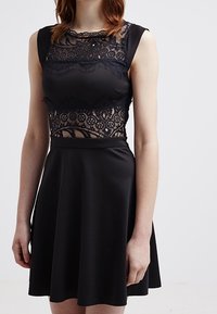 Czarna sukienka z koronkowym gorsetem i bezrękawowym krojem, z dopasowanym topem i rozkloszowanym dołem, o gładkiej fakturze i misternych detalach koronkowych.